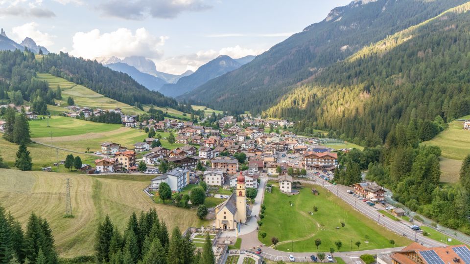 Drohnenblick auf Soraga di Fassa: Ein stilles Dorf zwischen See, Wiesen und Dolomiten, eingebettet in Ruhe pur.