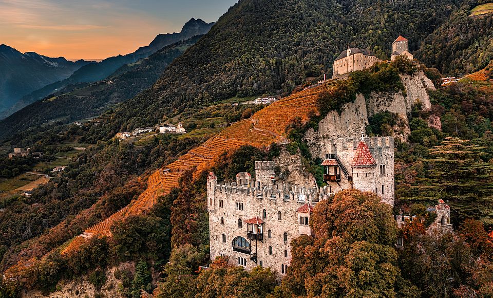 Goldener Herbst in Dorf Tirol: Weinberge leuchten in warmen Farben rund um das mächtige Schloss Tirol.