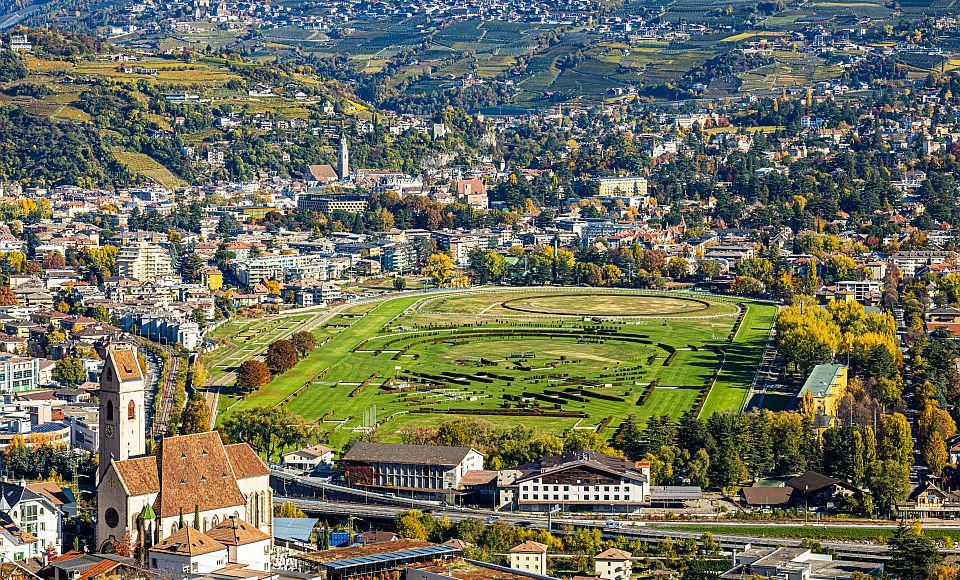 Drohnenblick auf Meran mit der traditionsreichen Pferderennbahn vor der eindrucksvollen Südtiroler Bergkulisse.