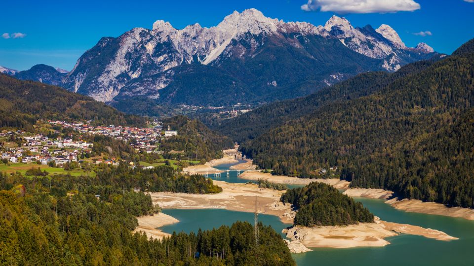 Der See Centro Cadore schimmert in verschiedenen Blautönen und spiegelt die umliegenden Berge wider.
