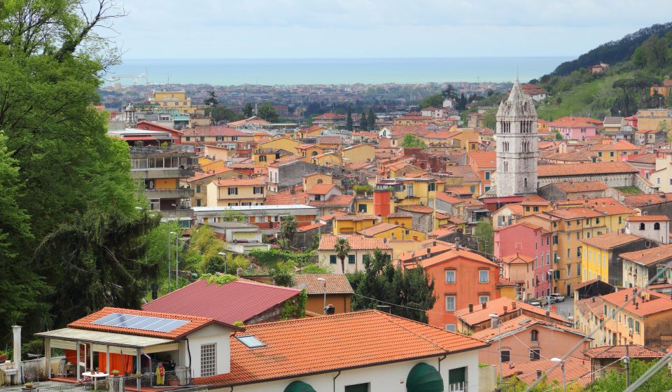 Ein Drohnenblick über Carrara zeigt die Kirchturmspitze des Doms vor dem Panorama heller Marmorberge und der verwinkelten Altstadt.