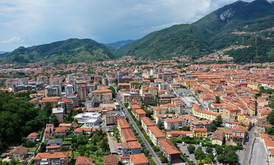 Massa, die Stadt an den Hügeln, zeigt sich im Drohnenblick eingebettet zwischen hellen Marmorbergen und Meer, mit klar erkennbarer historischer Silhouette.