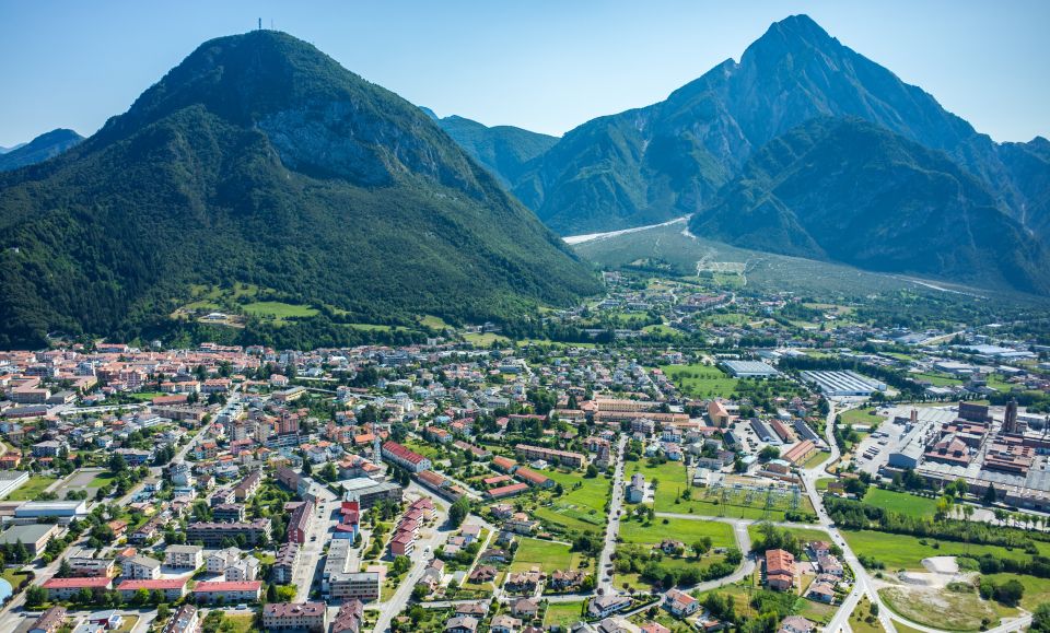 Drohnenblick auf Tolmezzo zeigt die Stadt im weiten Tal, umgeben von den Alpen, deren imposante Gipfel den Horizont dominieren.