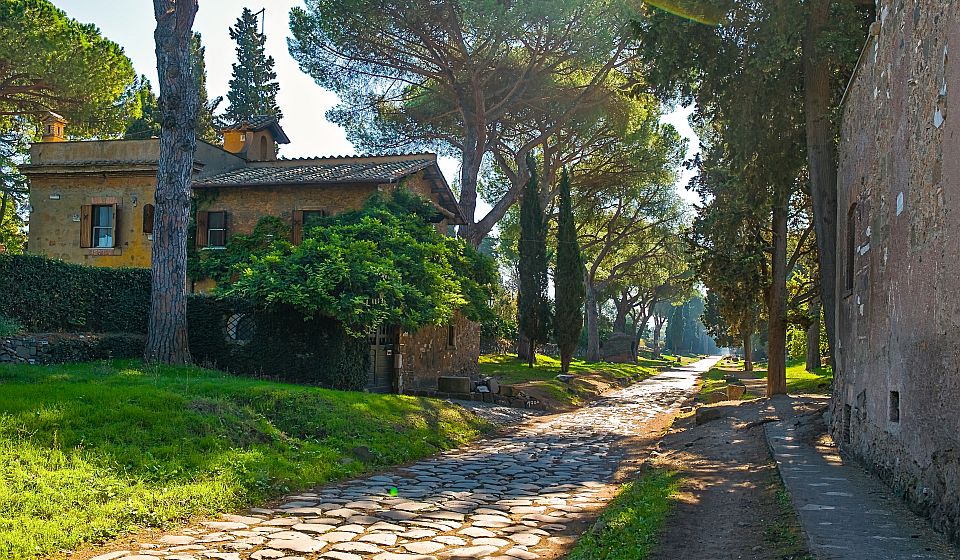 Die Via Appia Antica führt durch eine ruhige Landschaft mit historischen Grabmälern, Ruinen und Spuren aus römischer Zeit.