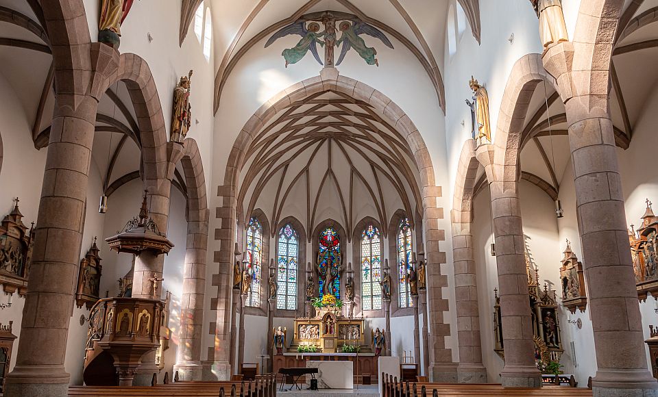 Im Inneren der Neuen Pfarrkirche beeindrucken Apostelfiguren, farbige Glasfenster und kunstvolle Details.