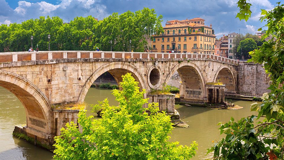 Historische Ponte Sisto über dem Tiber, umgeben von Bäumen und alten Gebäuden.